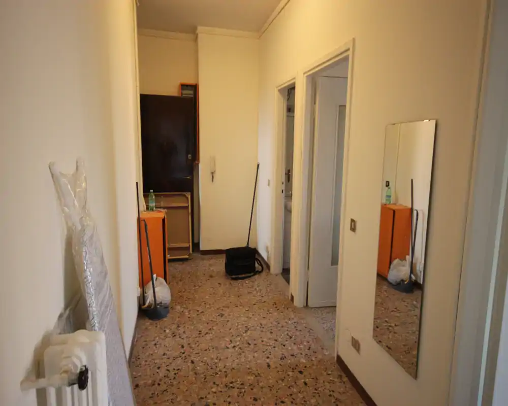 Bright entry hallway with terrazzo floor, wall-mounted mirror and an inner door; simple, functional space suitable for an apartment entrance.