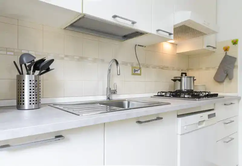 Bright modern kitchen with a stainless sink, gas hob and dishwasher. Clean countertops, utensil holder and tiled backsplash create a tidy, functional cooking area.