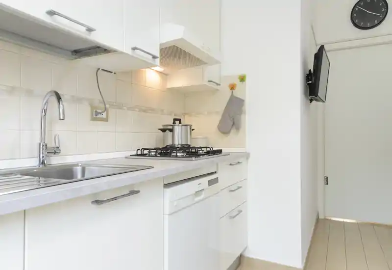 Bright, compact modern kitchen with a stainless sink, gas hob and integrated dishwasher. Clean white cabinetry and warm under-cabinet lighting create a tidy, functional space.