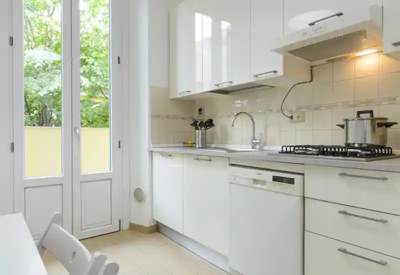 Bright modern kitchen with white cabinetry, gas hob, built-in dishwasher and a large glass door letting in abundant natural light.