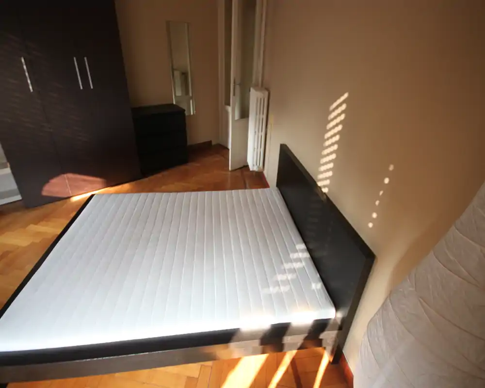 Camera da letto luminosa arredata con ampio letto matrimoniale e materasso, pavimento in parquet, armadio e comò; la luce naturale crea un'atmosfera accogliente.