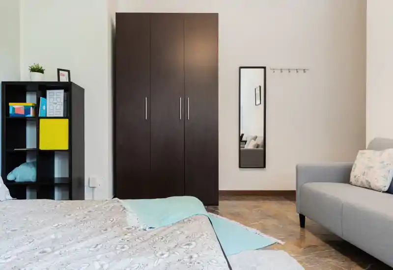 Dormitorio luminoso y ordenado con un gran armario, estantería abierta y cama parcialmente visible; textiles suaves y paleta neutra que crean un ambiente tranquilo.