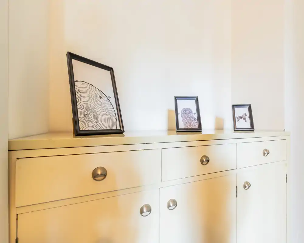 Bright entrance or hallway cabinet with framed prints on top; clean, minimal styling that suits an entryway or corridor.