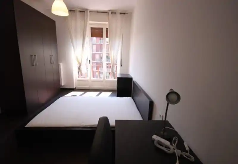 Dormitorio moderno y luminoso con cama baja de plataforma, armario, escritorio y una gran ventana que aporta mucha luz natural.