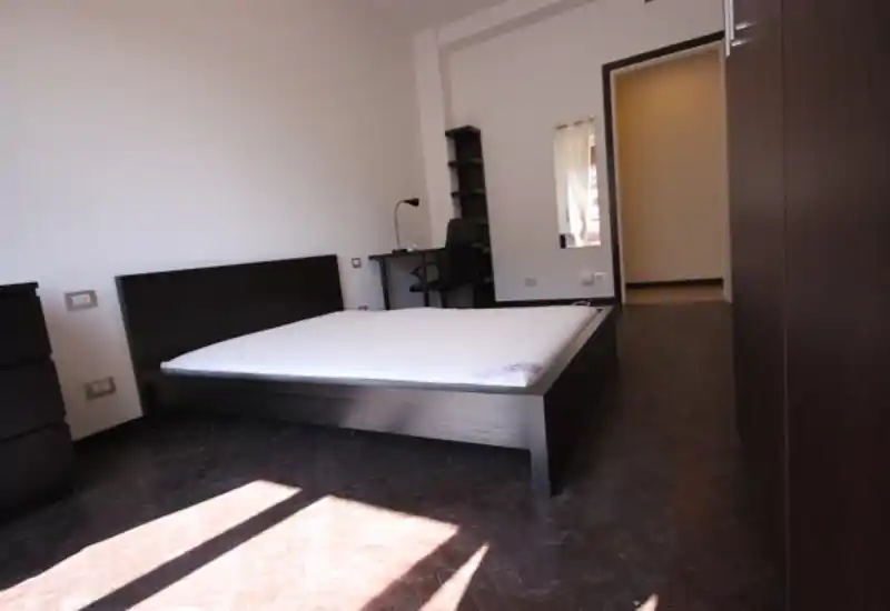 Dormitorio moderno y luminoso con cama doble en estructura de madera oscura, muebles a juego y un pequeño escritorio junto a la ventana que aporta abundante luz natural.