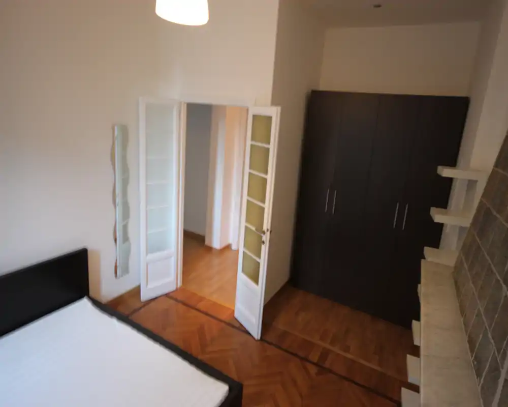 Camera da letto luminosa con letto matrimoniale, pavimento in parquet e un grande armadio scuro; pareti neutre e buona luce naturale rendono la stanza ariosa e funzionale per gli annunci.