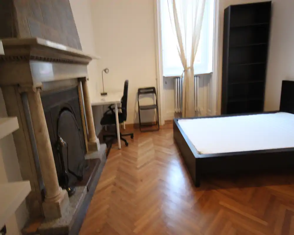 Camera da letto luminosa con letto basso, camino decorativo e pavimento in parquet; scrivania e scaffale offrono uno spazio funzionale.