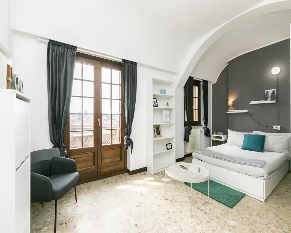 Camera da letto luminosa e di design con letto matrimoniale comodo, tessili morbidi e grandi porte-finestre che lasciano entrare molta luce naturale.
