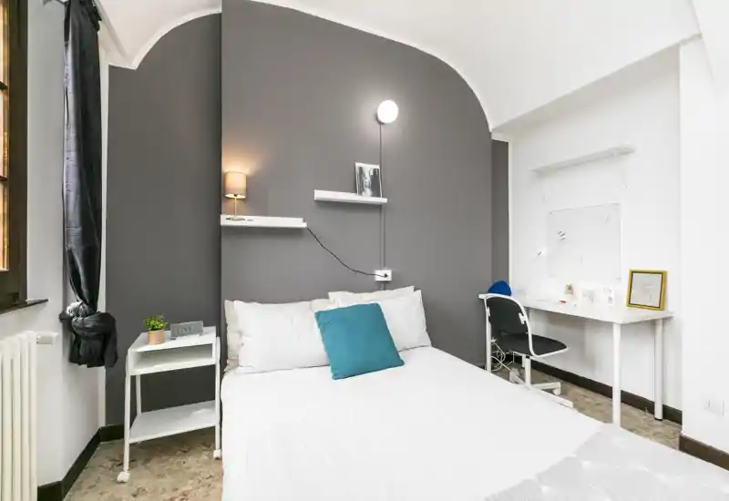 Bright, modern bedroom with a double bed against a dark accent wall, bedside table and a small desk — ideal for work and rest.