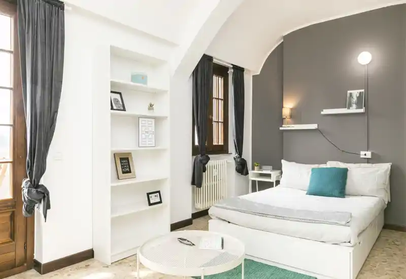 Bright, stylish bedroom with a neatly made double bed, soft textiles and natural light from tall windows. The neutral and teal accents create a calm, modern atmosphere ideal for rental listings.