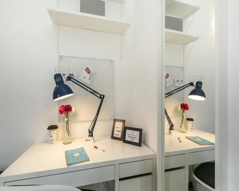 Well-styled workspace corner with a white desk, adjustable blue desk lamp, decorative flowers and framed quotes—bright and inviting for remote work or study.