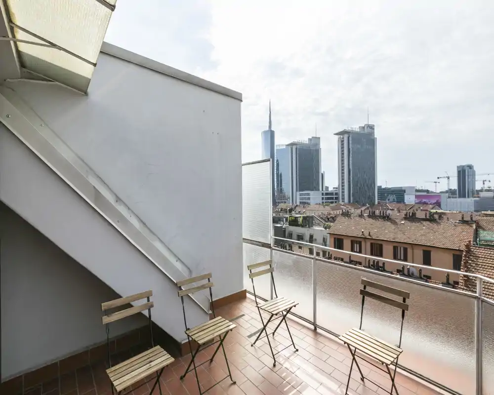 Sunny city balcony with terracotta tiles, simple folding chairs and a clear view over rooftops to modern skyscrapers — ideal for coffee or relaxing outdoors.