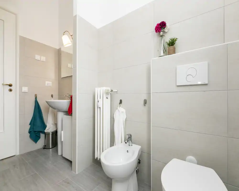Bright, modern bathroom with a wall-mounted toilet, bidet, small sink and neat tile finishes — clean, well-lit space ideal for rental listings.
