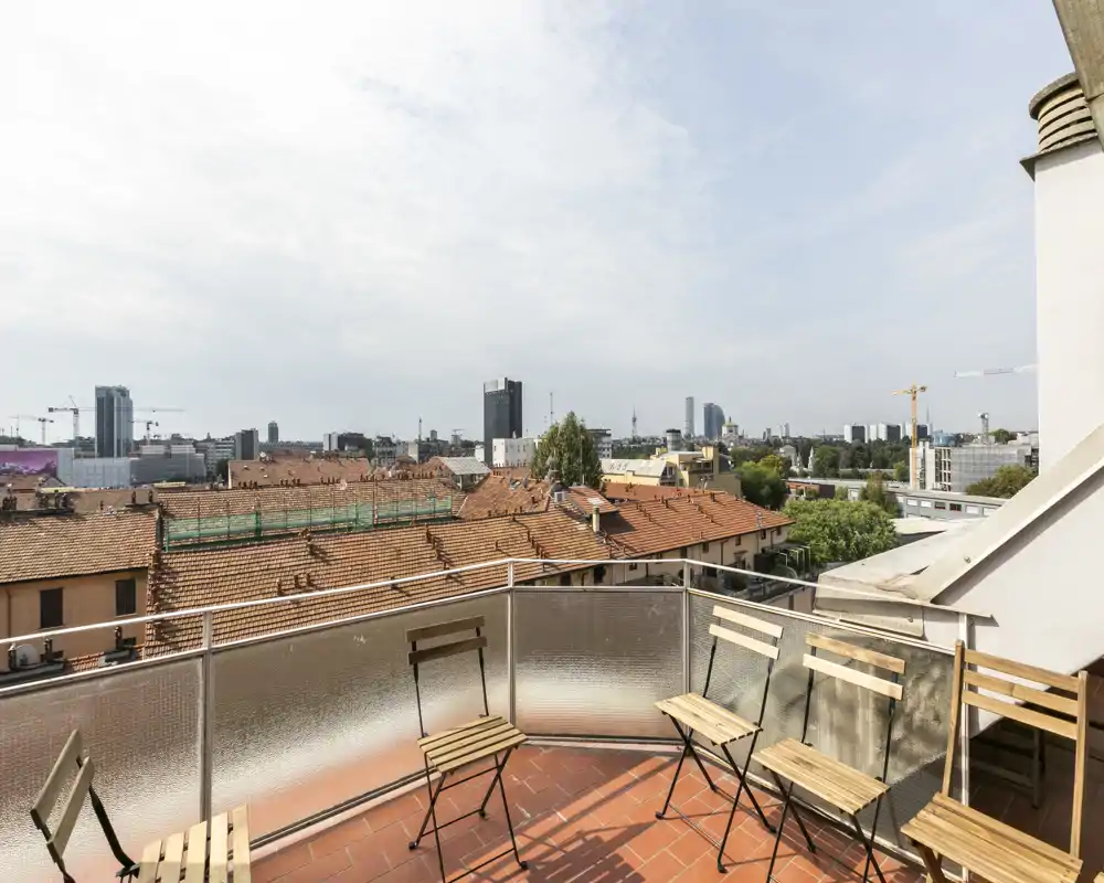 Sunny private terrace with city skyline views, tiled floor and folding wooden chairs — ideal for morning coffee or relaxing outdoors.