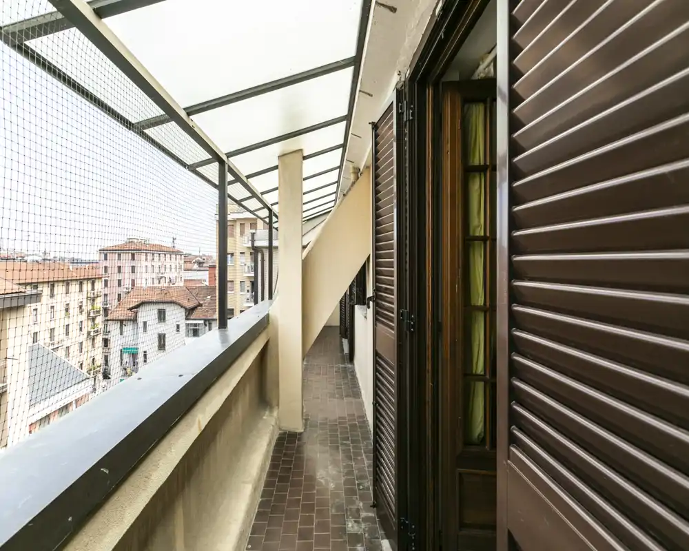Covered balcony with tiled floor, protective netting and a partial city view — a narrow outdoor corridor ideal for morning coffee or drying laundry.
