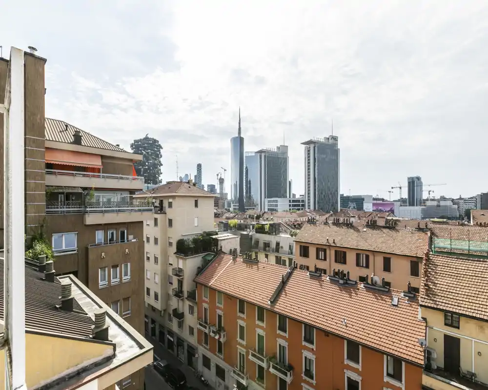 Sunny urban terrace view overlooking neighboring rooftops and a distant skyline with modern high-rises — ideal for listing a balcony or top-floor apartment with city views.