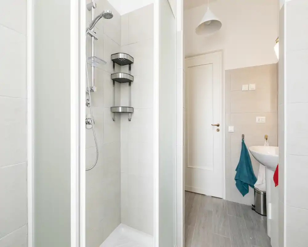 Bright, modern bathroom with a tiled shower cubicle, wall-mounted shower and a compact sink — clean, minimal lines and neutral tones.