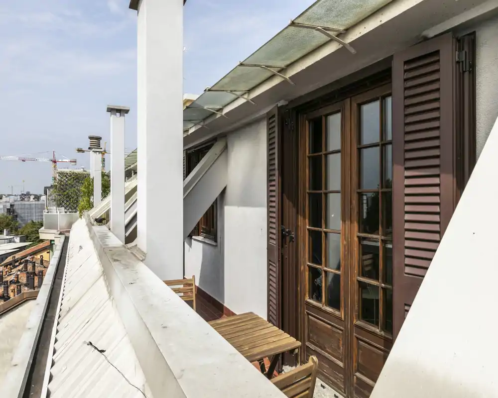 Sunny narrow balcony with wooden folding chairs and a small table, overlooking city rooftops — ideal for morning coffee.