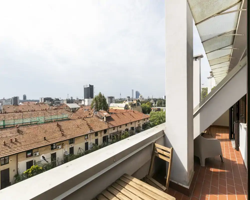 Sunny private balcony with terracotta tiles, a small wooden folding chair and panoramic city views — ideal for morning coffee.