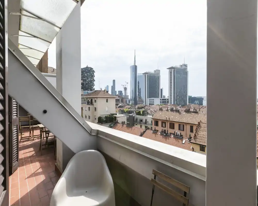 Sunny balcony with seating and a clear city view; small table and chair visible on a tiled floor, ideal for morning coffee overlooking the skyline.