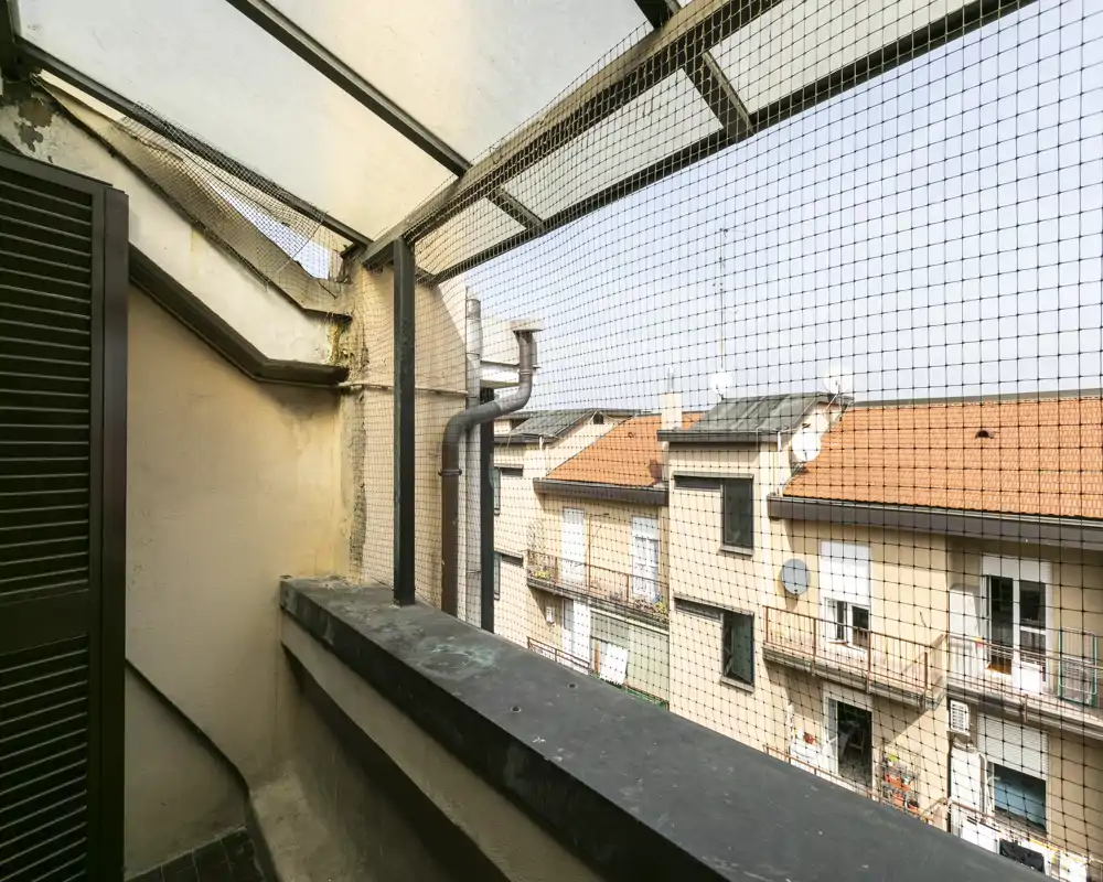 Small enclosed balcony with protective mesh and a view over neighboring rooftops; practical outdoor space for airing or placing plants.