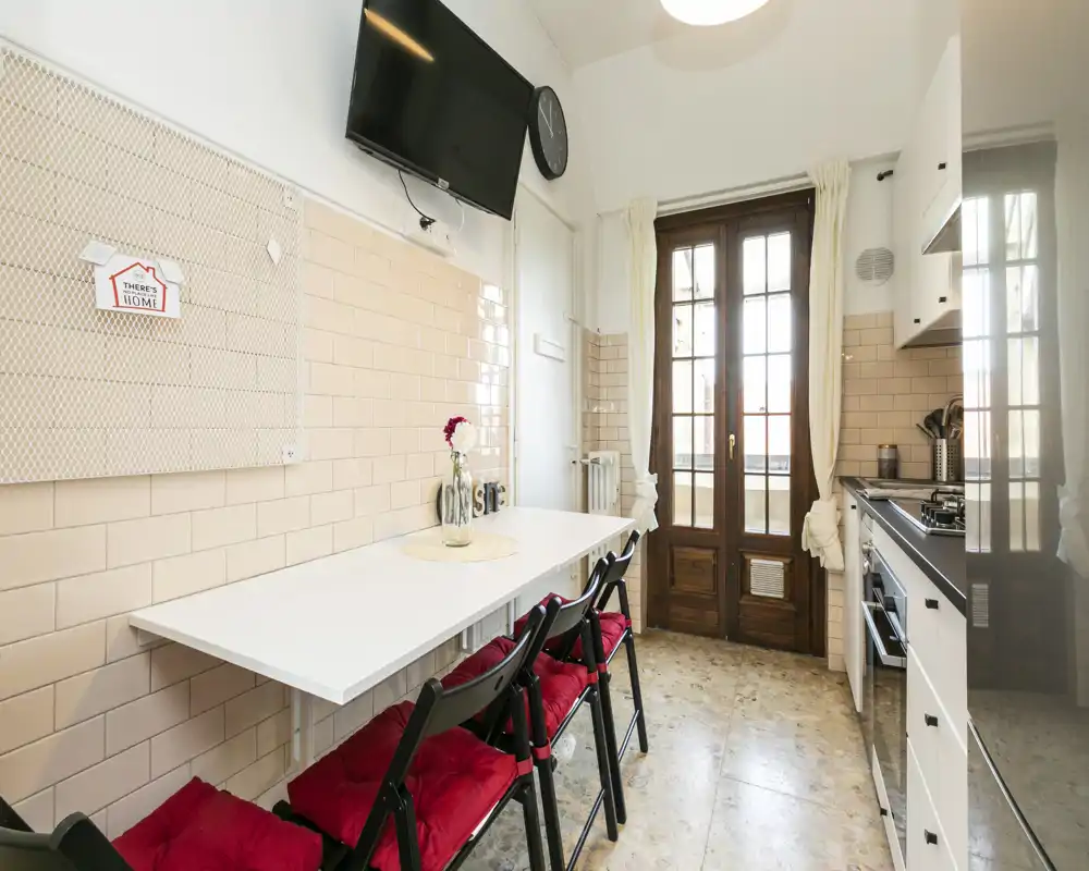 Bright, well-styled kitchen with a fold-down white table, red-cushioned chairs and a wood-framed glass door letting in natural light.