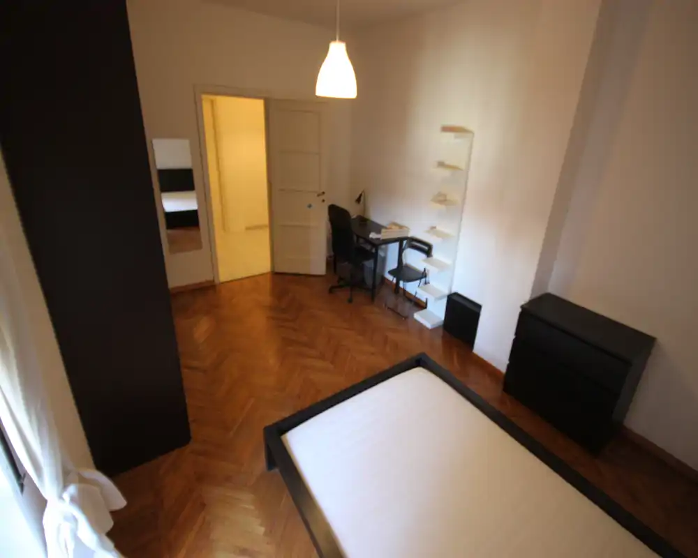 Dormitorio luminoso y minimalista con cama doble, suelo de parquet y una pequeña zona de escritorio; luz natural y diseño adecuado para alquileres.