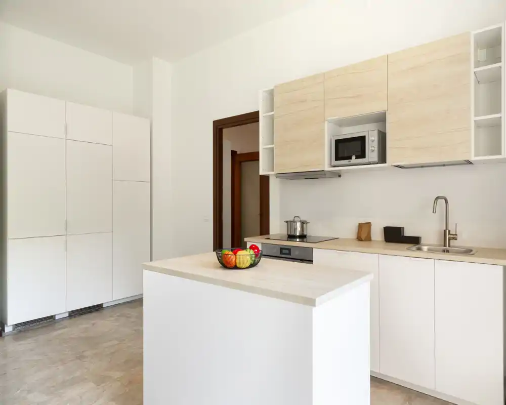 Cocina moderna y luminosa con isla central, muebles de madera clara, electrodomésticos integrados y un cuenco de fruta decorativo — ideal para anuncios que destaquen estilo y funcionalidad.