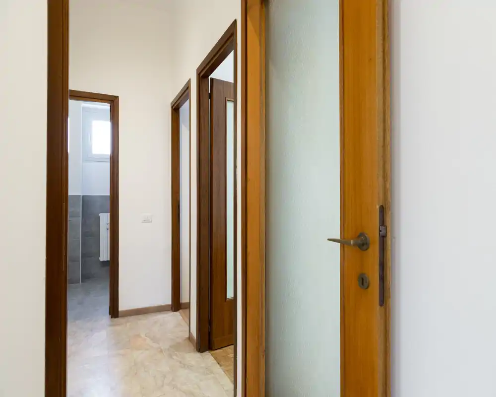 Recibidor luminoso y neutro con puertas de madera y suelo de baldosas; pasillo bien iluminado que muestra varias puertas y acabados limpios y sencillos.