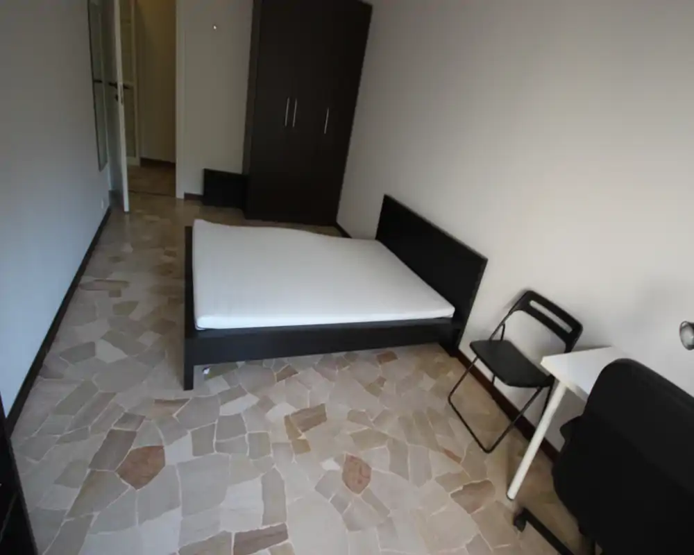 Camera da letto luminosa e minimal con letto matrimoniale su struttura bassa scura, armadio e una piccola scrivania — semplice, pulita e pronta per gli ospiti.