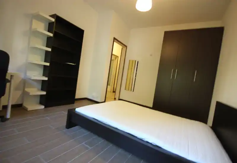 Camera da letto moderna e luminosa con letto basso, ampio armadio e scaffalatura: ambiente ordinato, essenziale e ben illuminato.