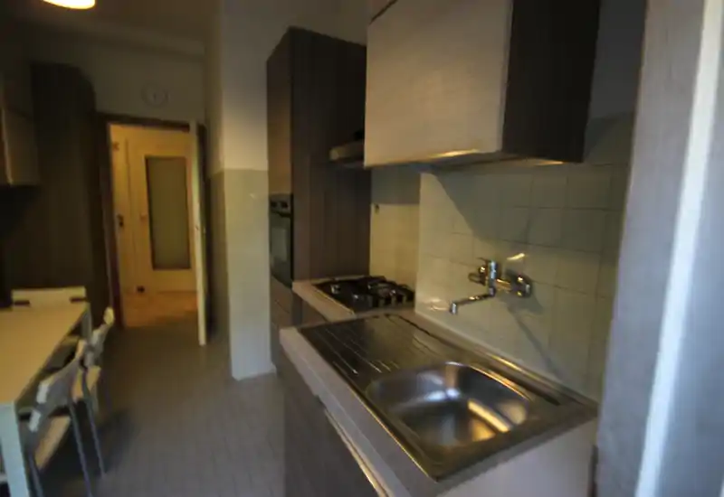 Cucina a corridoio funzionale con lavello in acciaio, piano cottura a gas e forno incassato; piccolo angolo pranzo con sedie, pratica per l'uso quotidiano.