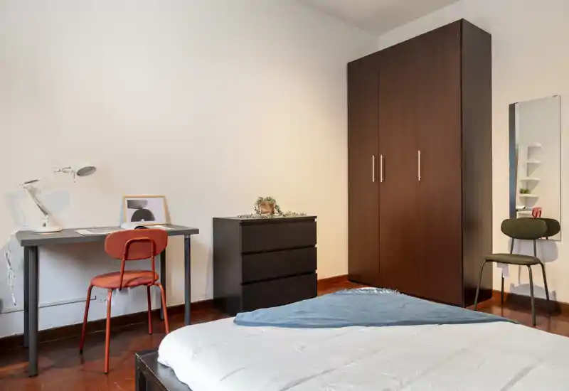 Dormitorio luminoso y de estilo sencillo con cama en primer plano, escritorio y silla, armario y cómoda — ideal para una sola persona o estudiante.