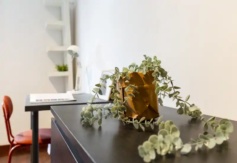 Rincón acogedor de la sala con una planta colgante sobre una superficie de madera oscura, una lámpara de escritorio y una silla roja al fondo — luminoso y estilizado.