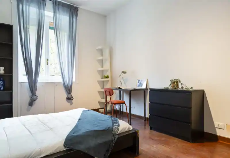 Dormitorio luminoso y de estilo sencillo con cama doble cómoda, luz natural desde la ventana con cortinas, un pequeño escritorio y cómoda — ideal para trabajar y relajarse.