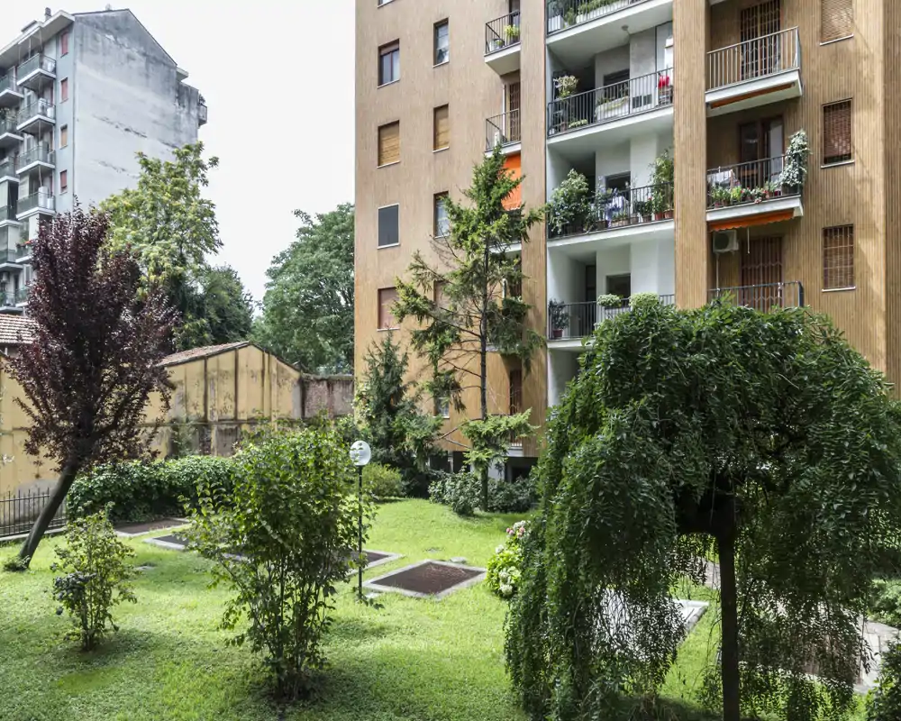 Patio comunitario con césped, pequeños árboles ornamentales y apartamentos con balcones que dan al espacio verde.