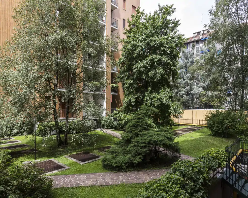 Patio interior bien cuidado con árboles maduros, césped y senderos pavimentados: un espacio verde tranquilo dentro del complejo de apartamentos.