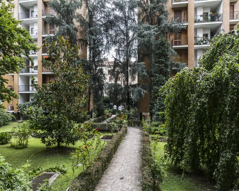 Jardin de cour privé avec allée centrale pavée, haies taillées, arbres matures et balcons d'appartements alentour — espace vert calme au cœur de l'immeuble.