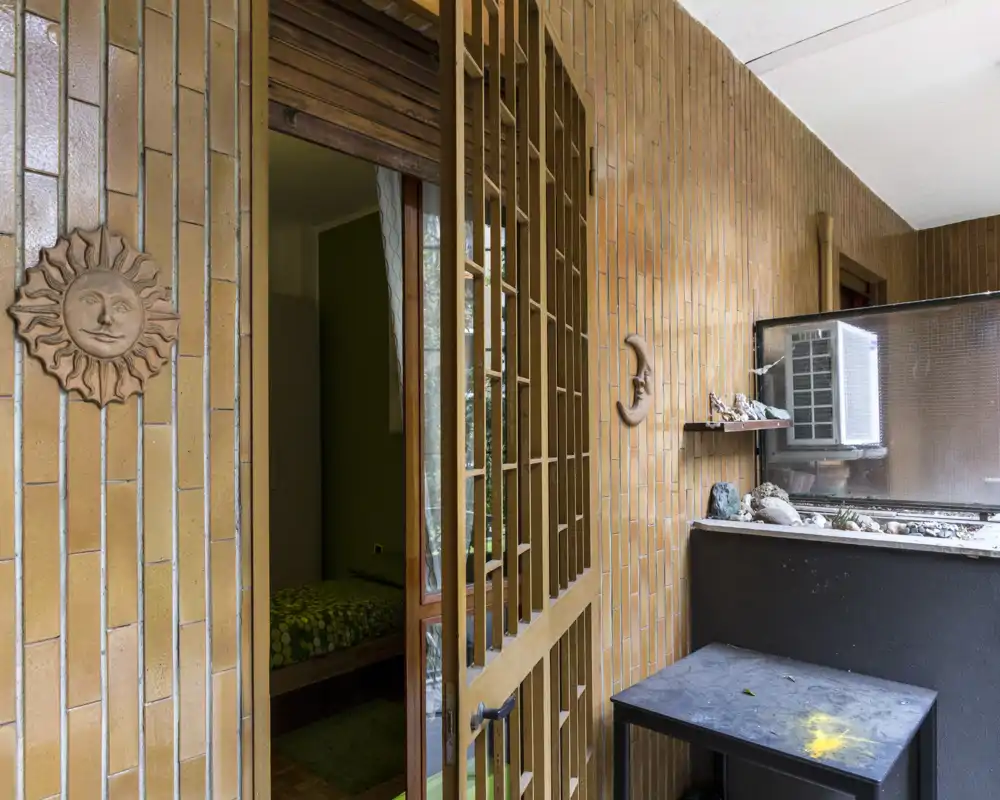 Vue sur une petite chambre depuis le balcon; le lit avec une housse à motifs est visible à travers l’encadrement et la lumière naturelle éclaire la pièce.