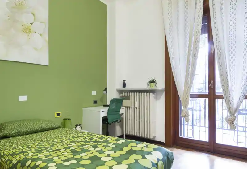 Chambre lumineuse aux accents verts, lit simple, bureau et porte-fenêtre laissant entrer beaucoup de lumière naturelle ; moderne, propre et idéale pour des locations courtes.