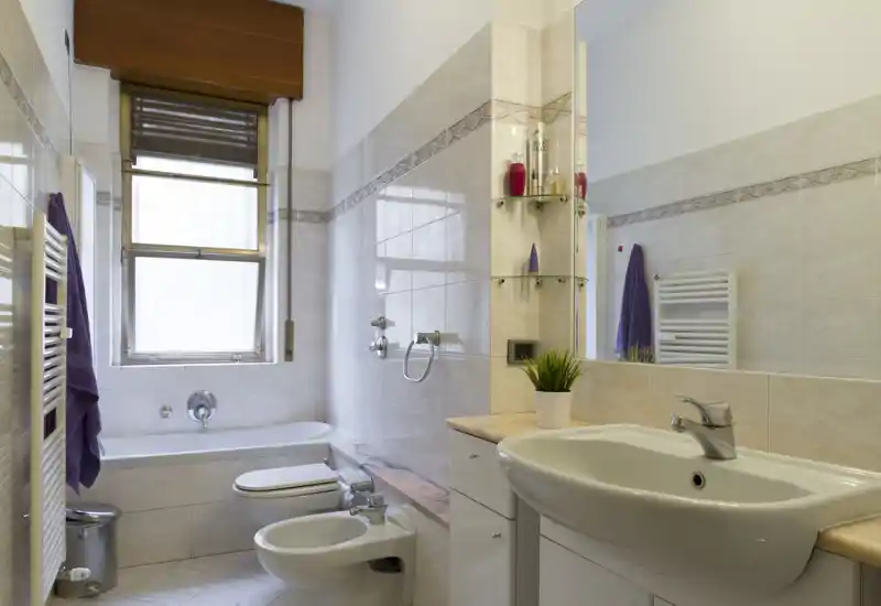 Bright, well-maintained bathroom with a bathtub, bidet, toilet and sink; neutral tiles and a large mirror create a spacious feel.
