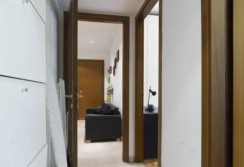 Bright, tidy entrance corridor with visible front door and a small seating area; clean walls and practical storage along the left wall.
