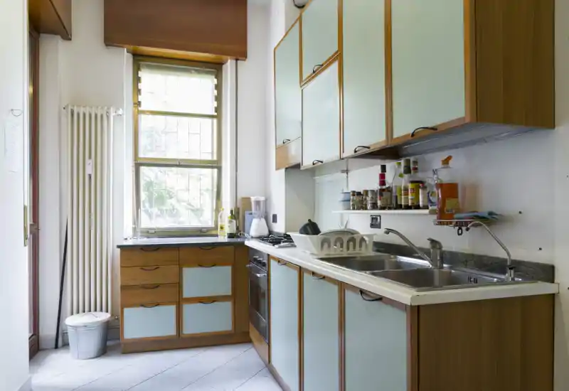 Bright, compact kitchen with wooden cabinets and mint-colored doors, double sink, gas stove and a window providing natural light.
