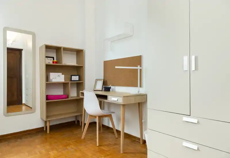 Angolo di camera luminoso con scrivania in legno, sedia, libreria e armadio capiente — ideale come zona studio nella camera da letto.