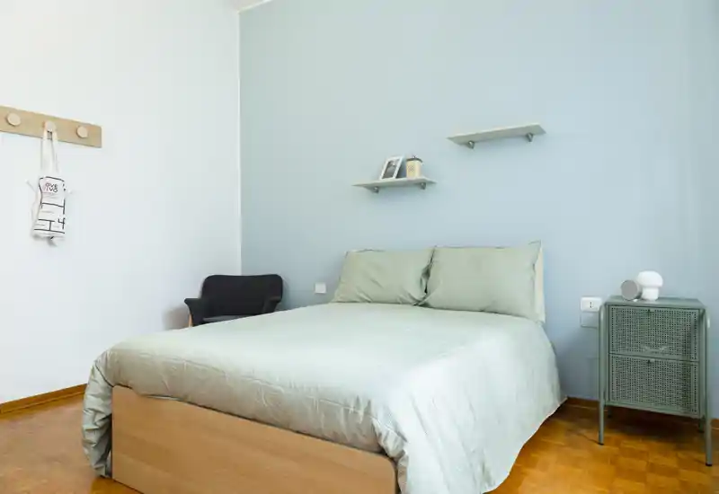 Chambre lumineuse et soignée avec un lit double en linge pastel, une table de chevet et des étagères murales minimalistes pour un rangement discret.