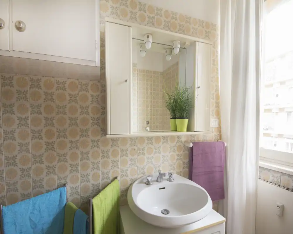 Bagno luminoso con lavabo rotondo, pensile con specchio e piastrelle vintage a motivi; asciugamani colorati che aggiungono un tocco accogliente.