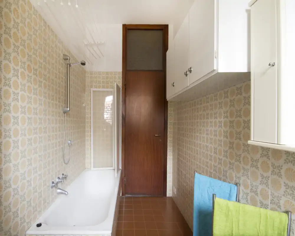 Bagno in stile retrò con vasca e doccia a soffitto, piastrelle decorate e pensili a muro; spazio compatto e ben illuminato adatto a annunci immobiliari.