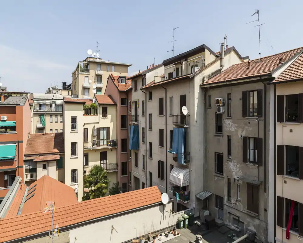 Cortile interno soleggiato e facciate degli appartamenti con tetti in terracotta e balconi — chiara vista esterna urbana.