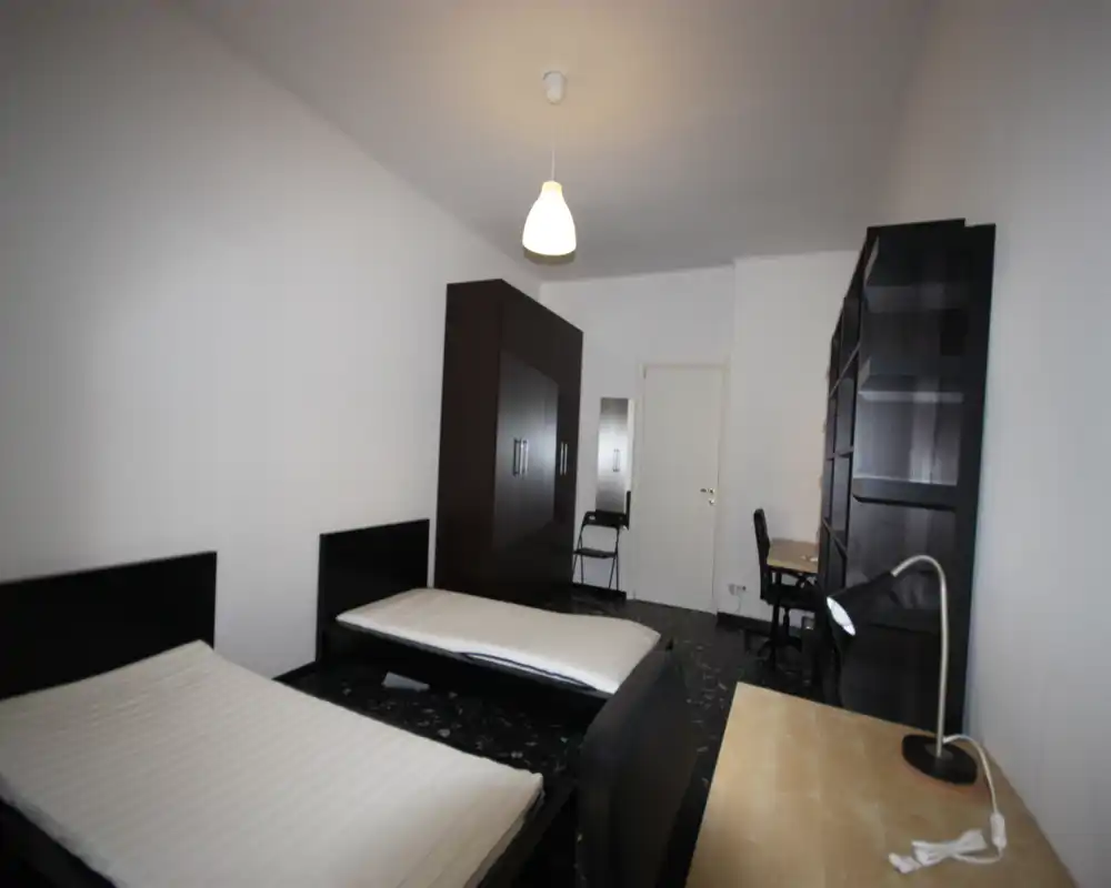 Dormitorio luminoso con dos camas individuales, un gran armario, escritorio y estanterías: distribución funcional ideal para estudiantes o compañeros de piso.