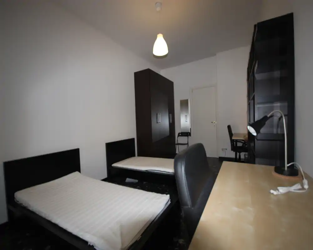 Amplia habitación con dos camas individuales, un gran armario y un escritorio. Distribución sencilla y ordenada, ideal para estudiantes o compañeros de piso.